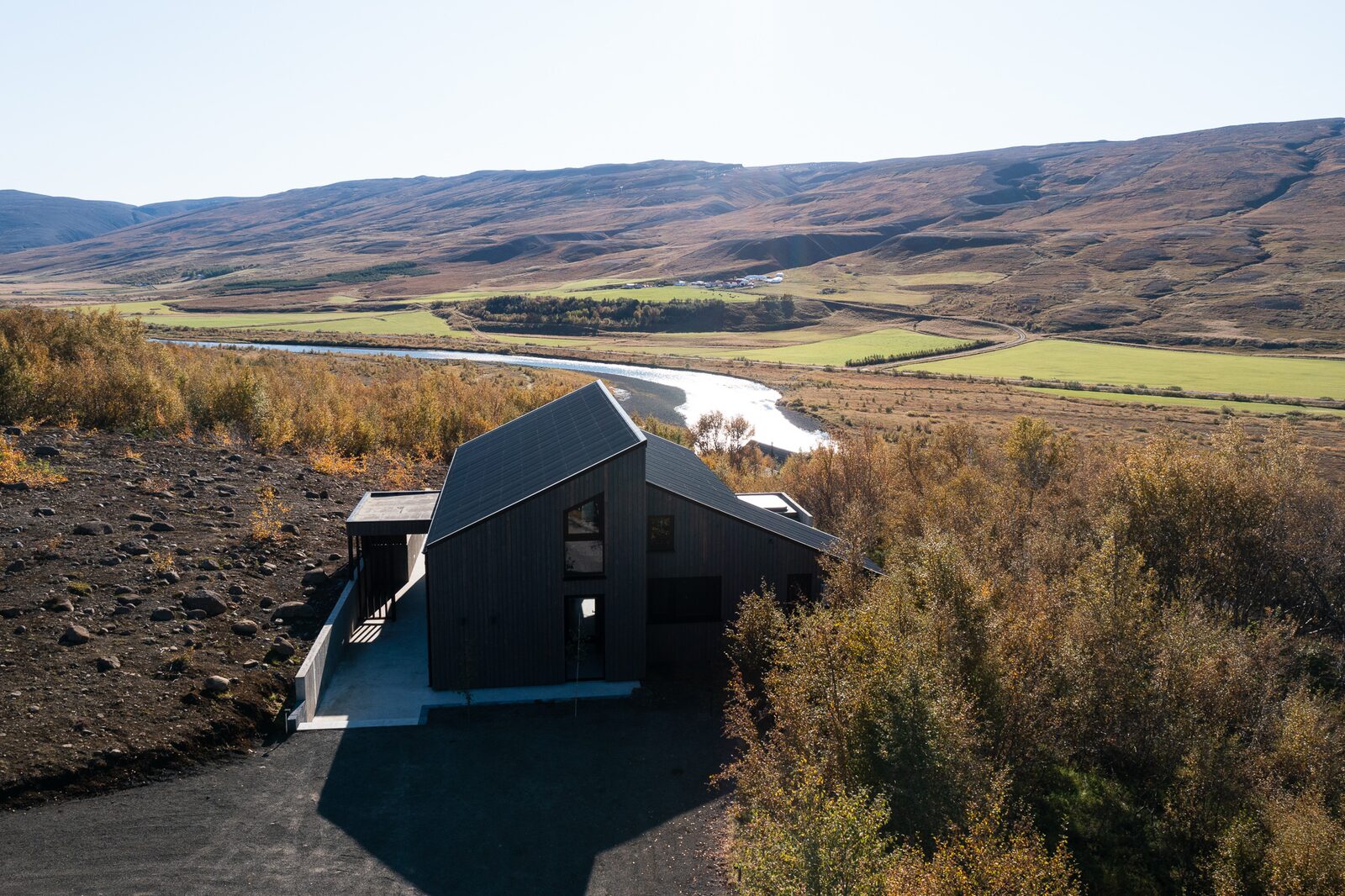 A drone view of the dark timber-clad house set low against a canyon hillside, autumn colours across the landscape.