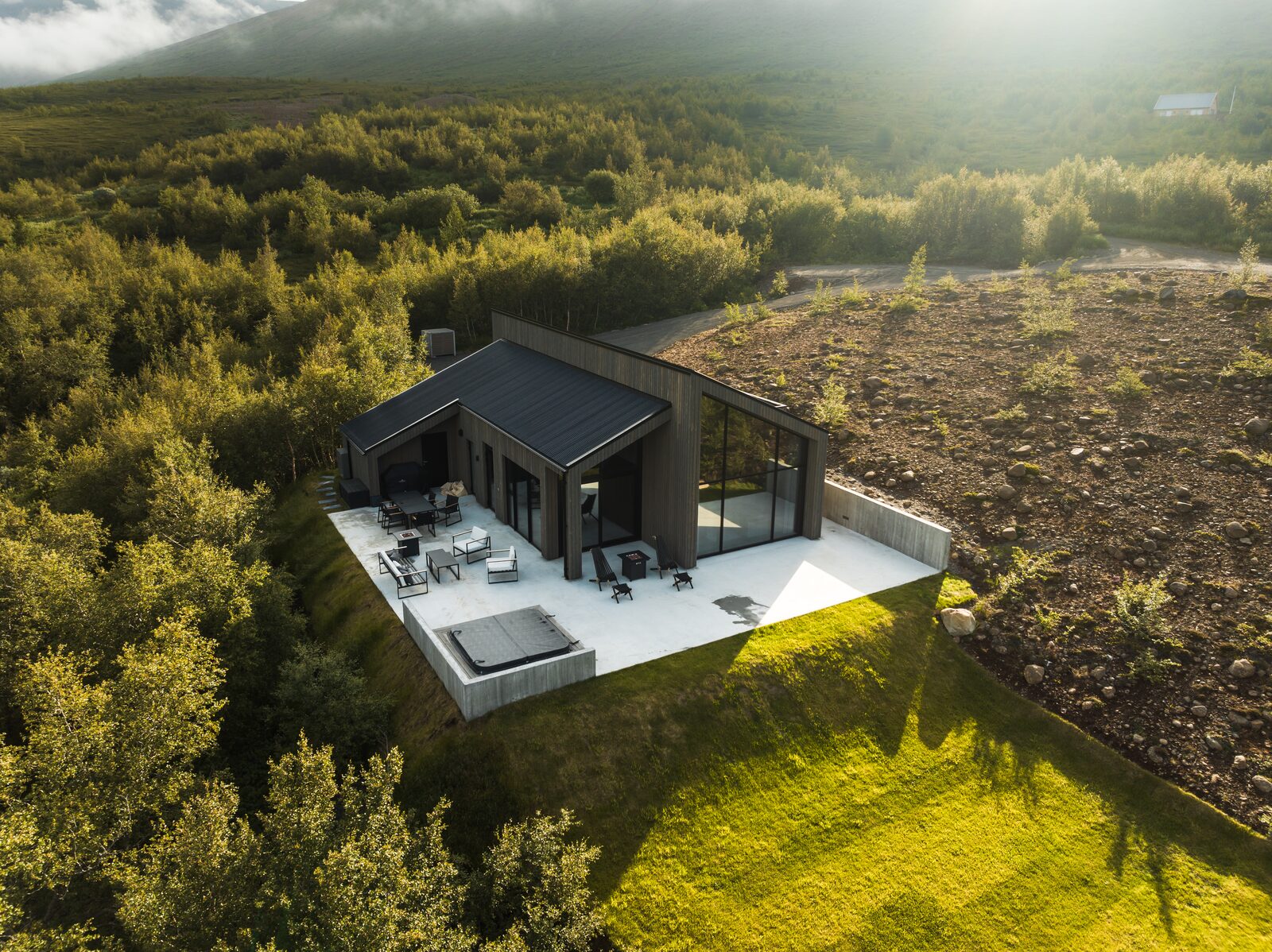 A drone view over surrounding birch forest to the house and its terrace, hot tub visible alongside.
