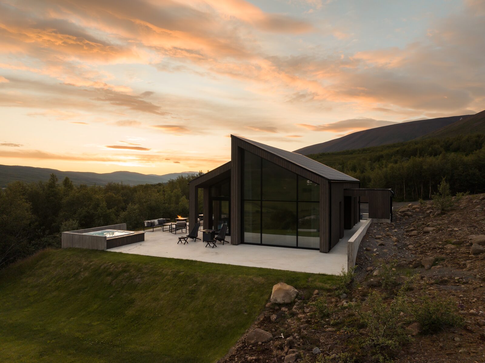 A drone view of the house and terrace furniture at golden hour, dramatic clouds lit orange and pink overhead.