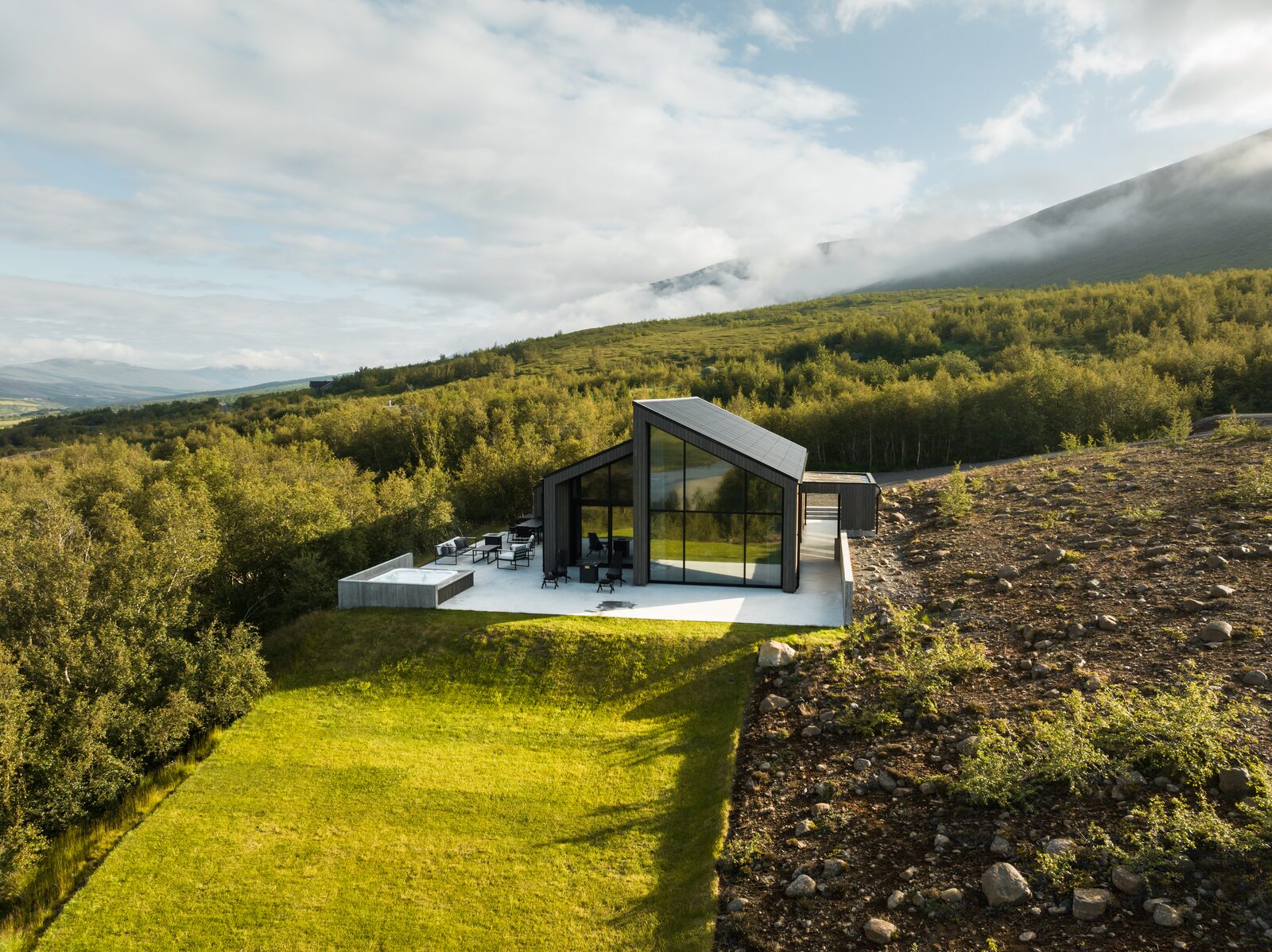 A drone view of the house and terrace with the hot tub, golden sunset light and long shadows across the hillside.