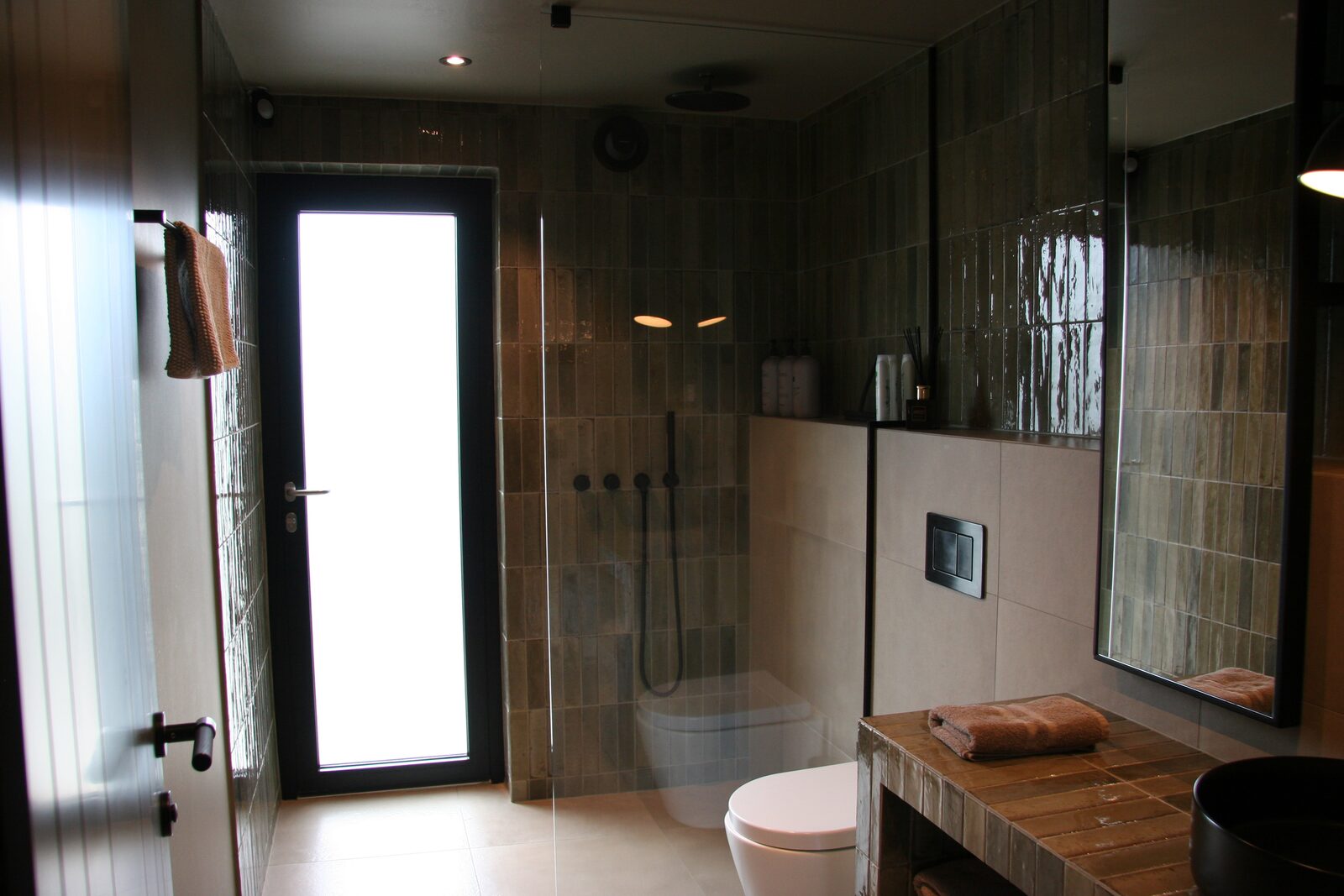 The bathroom seen from the shower end, with a glazed exterior door letting in daylight beside the tiled shower stall.