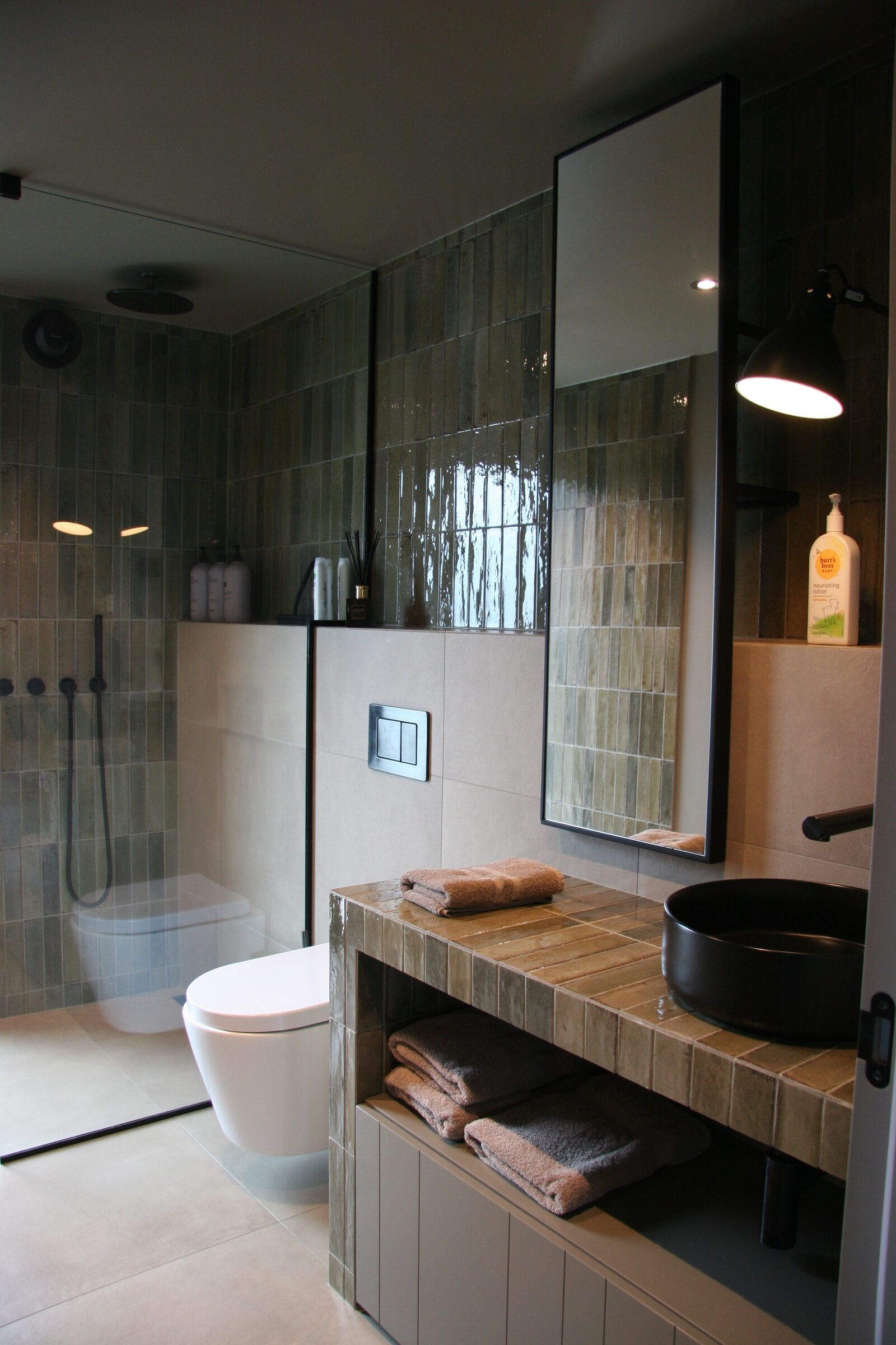 A walk-in shower behind glass next to a stone-topped vanity with a round black basin and folded towels.
