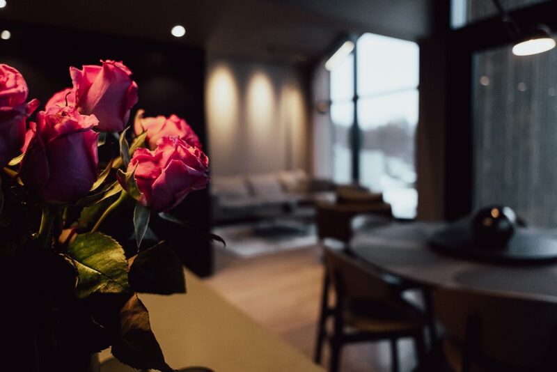 A dining table set with cutlery and a vase of red roses in the foreground, the room softly lit and out of focus behind.