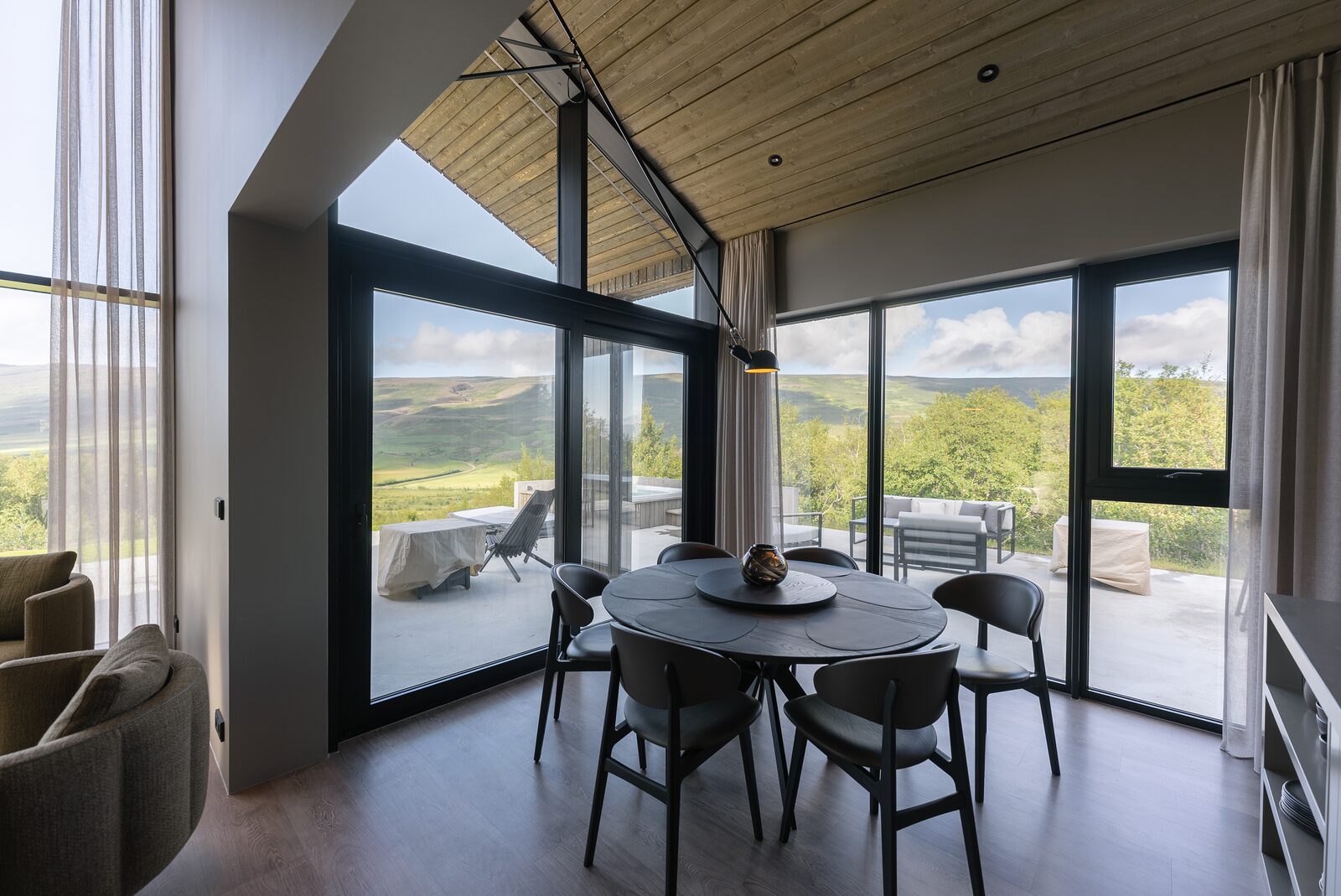 A round dining table set for two beside a full-height window, daylight and the valley visible outside.