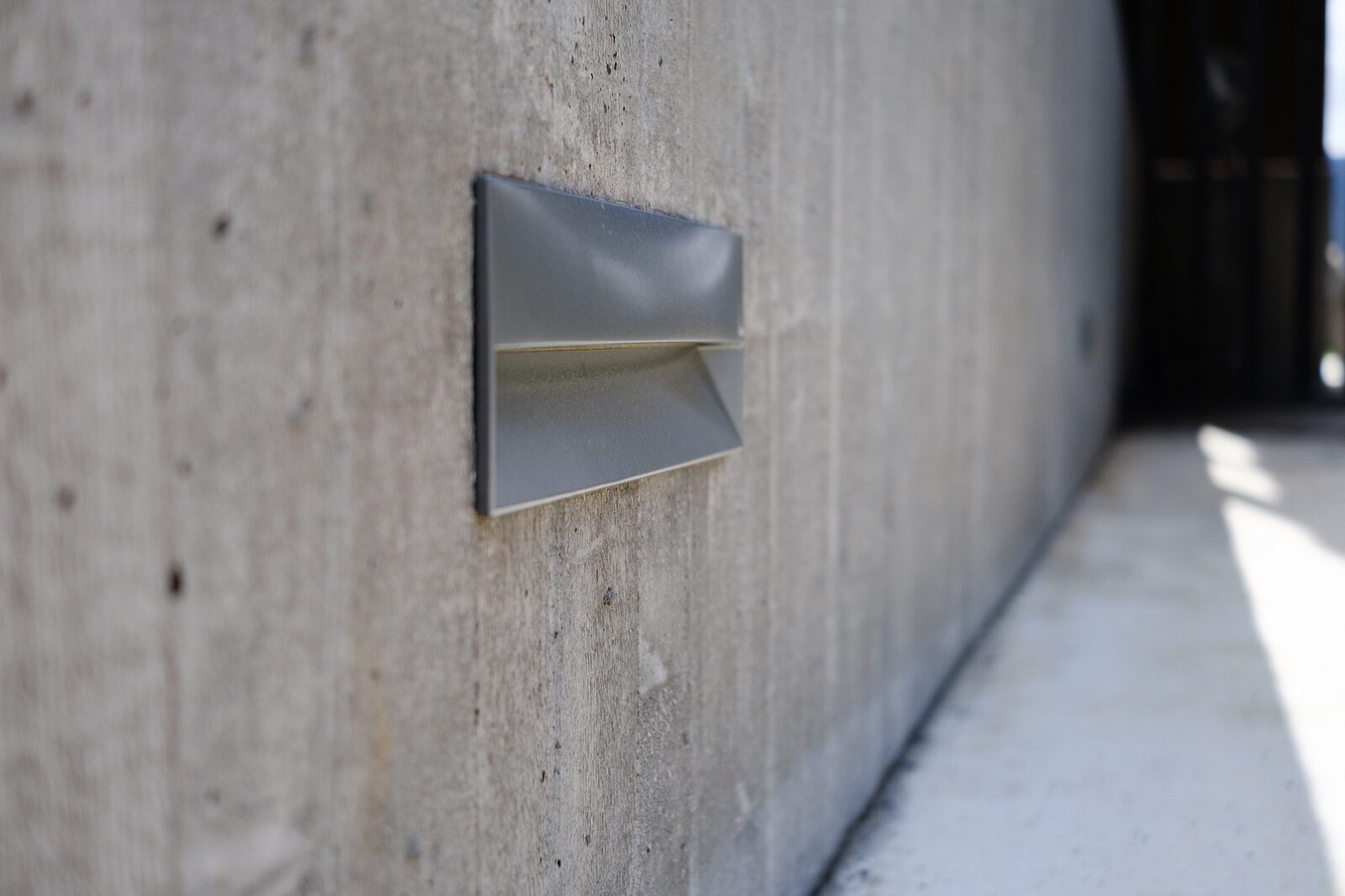 A small triangular wall light fixture set into a board-formed concrete wall.