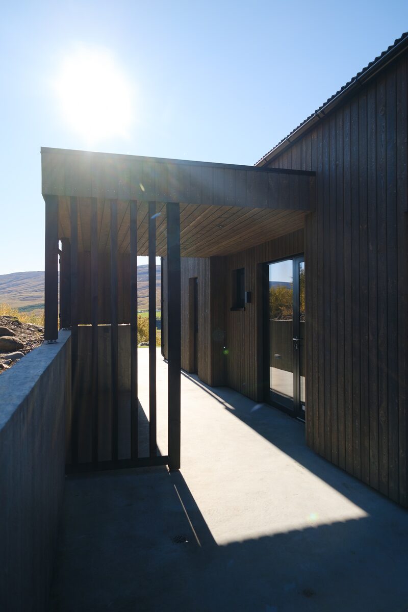 A covered concrete walkway along the side of the house with strong sun flare and shadow.
