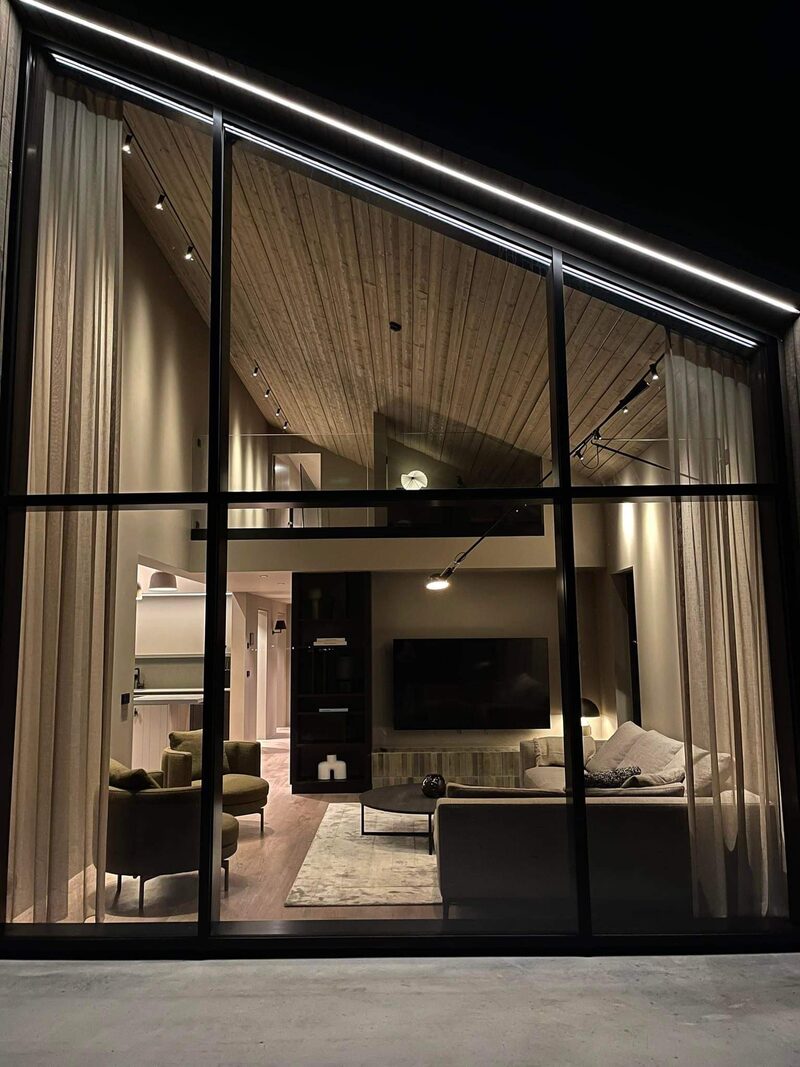 The living room and TV wall glowing through the tall glass gable at night.