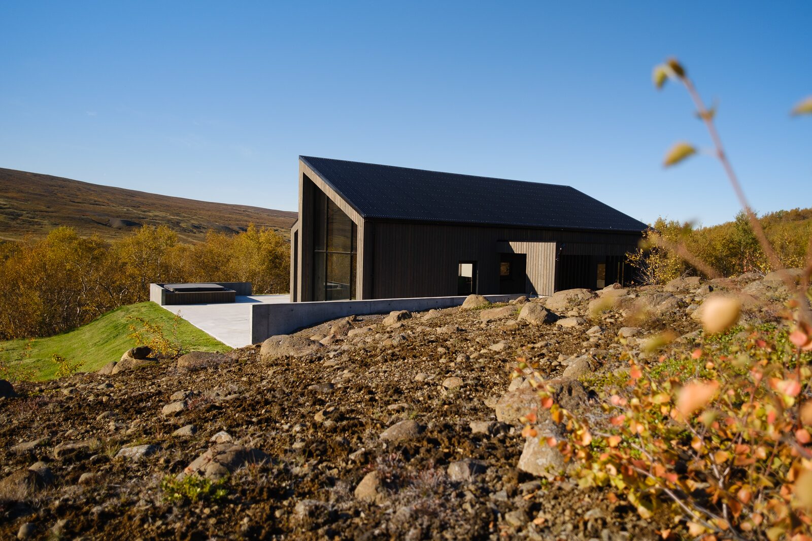 The house seen from a distance on its hillside plot, rocky ground in the foreground.