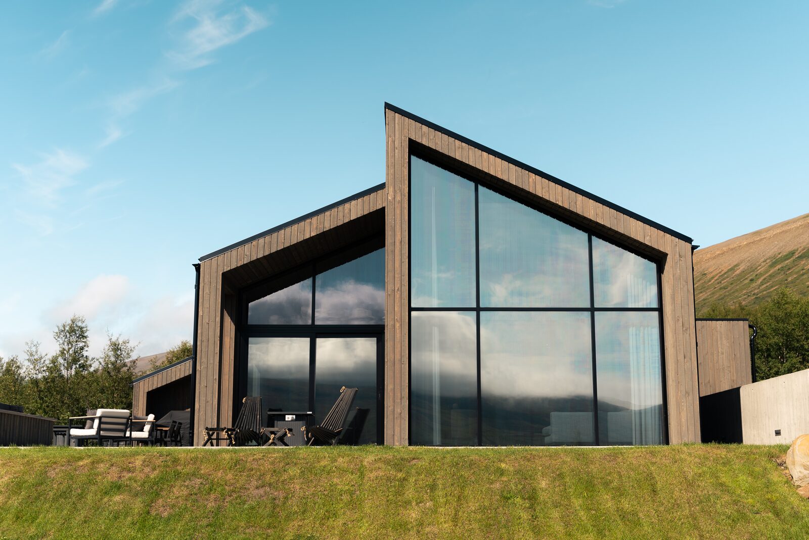 The full house on its grass plot in daylight, hills and outdoor furniture visible.