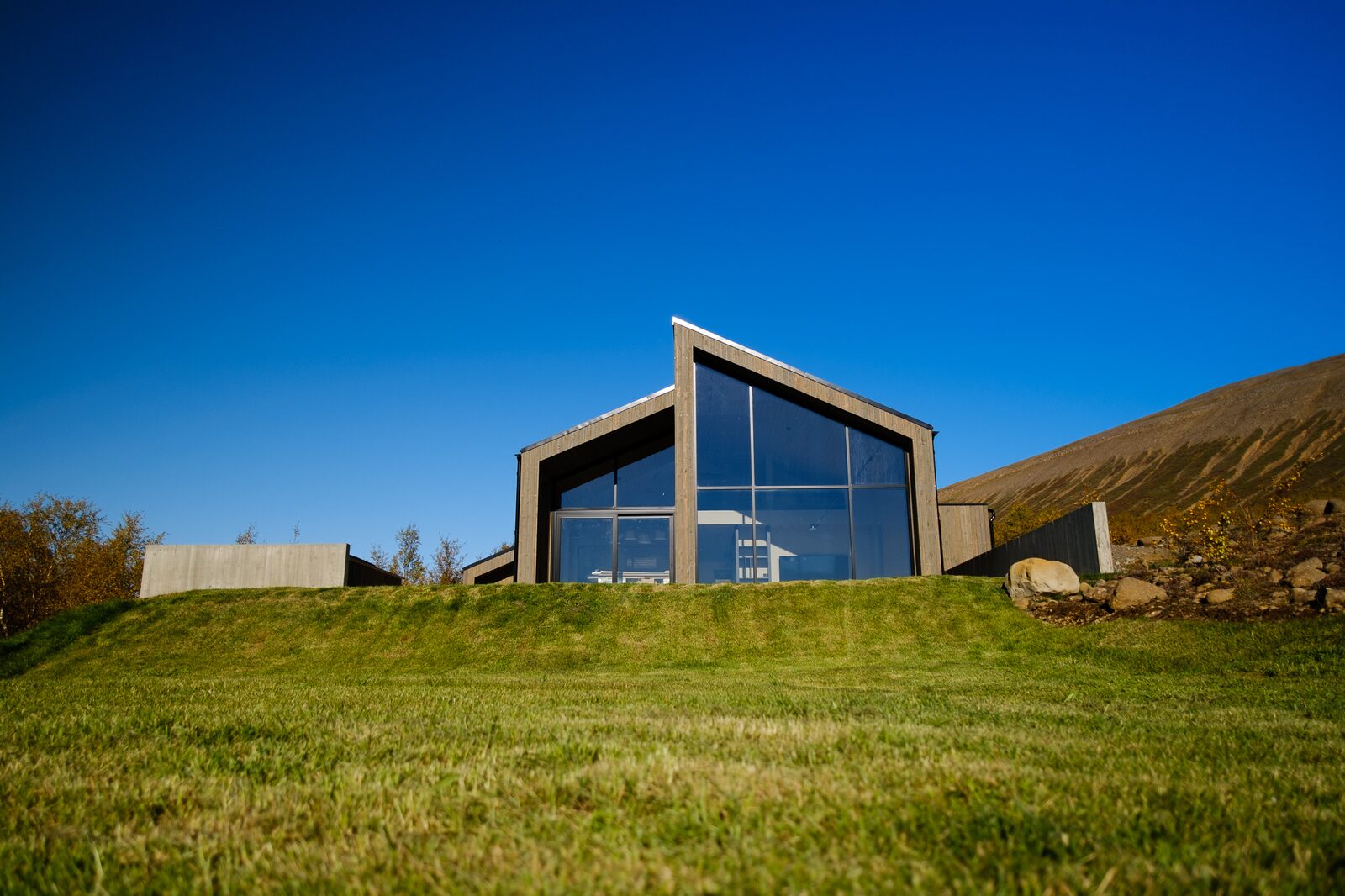 A wide daytime view of the house on its grass plot with hills behind under a clear sky.