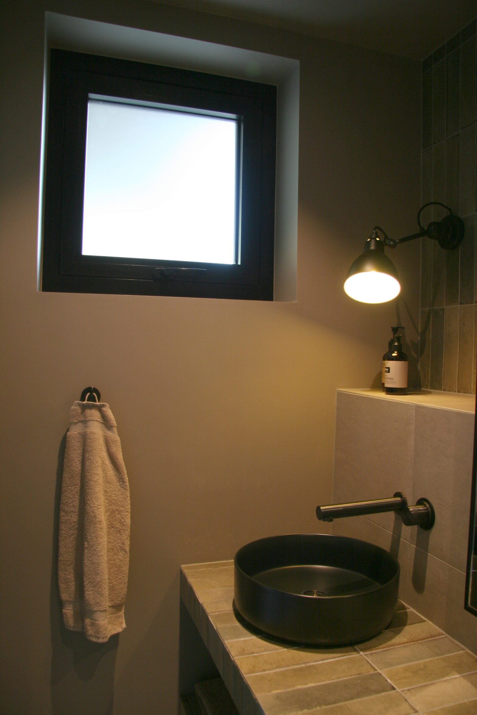 A round black vessel sink on a raw-edged wood shelf below a small window, with a hand towel on a hook.