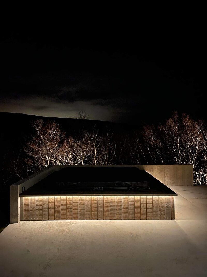 The covered hot tub lit up at dusk, bare birch branches lit against the dark hillside behind.