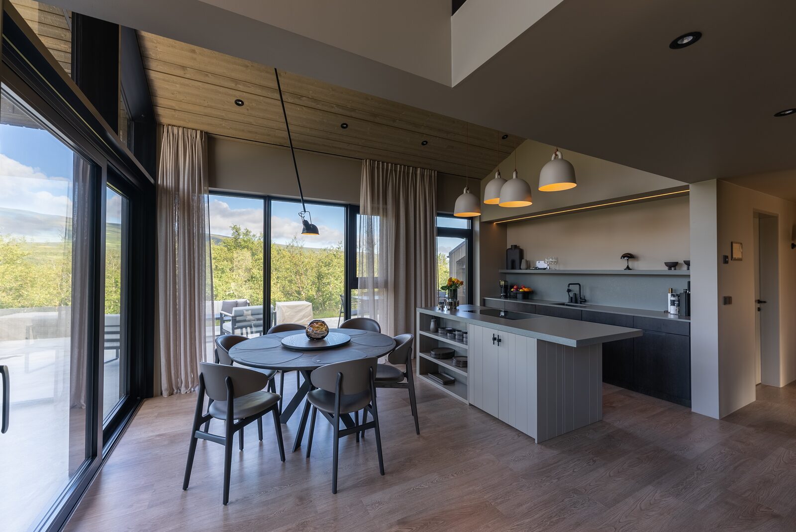The kitchen and dining area at dusk, warm pendant light against deep blue evening light through the windows.