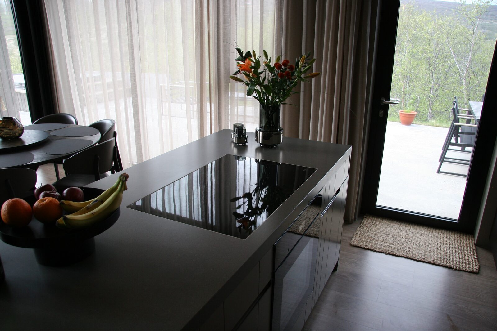 A dark kitchen island with a bowl of fruit and a vase of flowers, the front door and entry mat visible beyond.