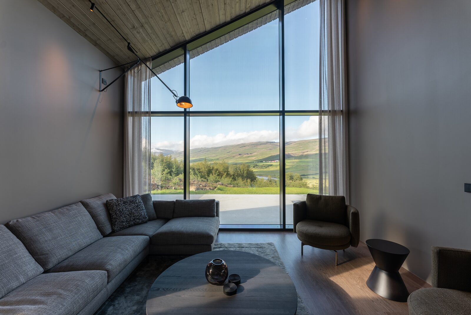 A closer angle on the living room sofa and round side table, sheer curtains framing the window.