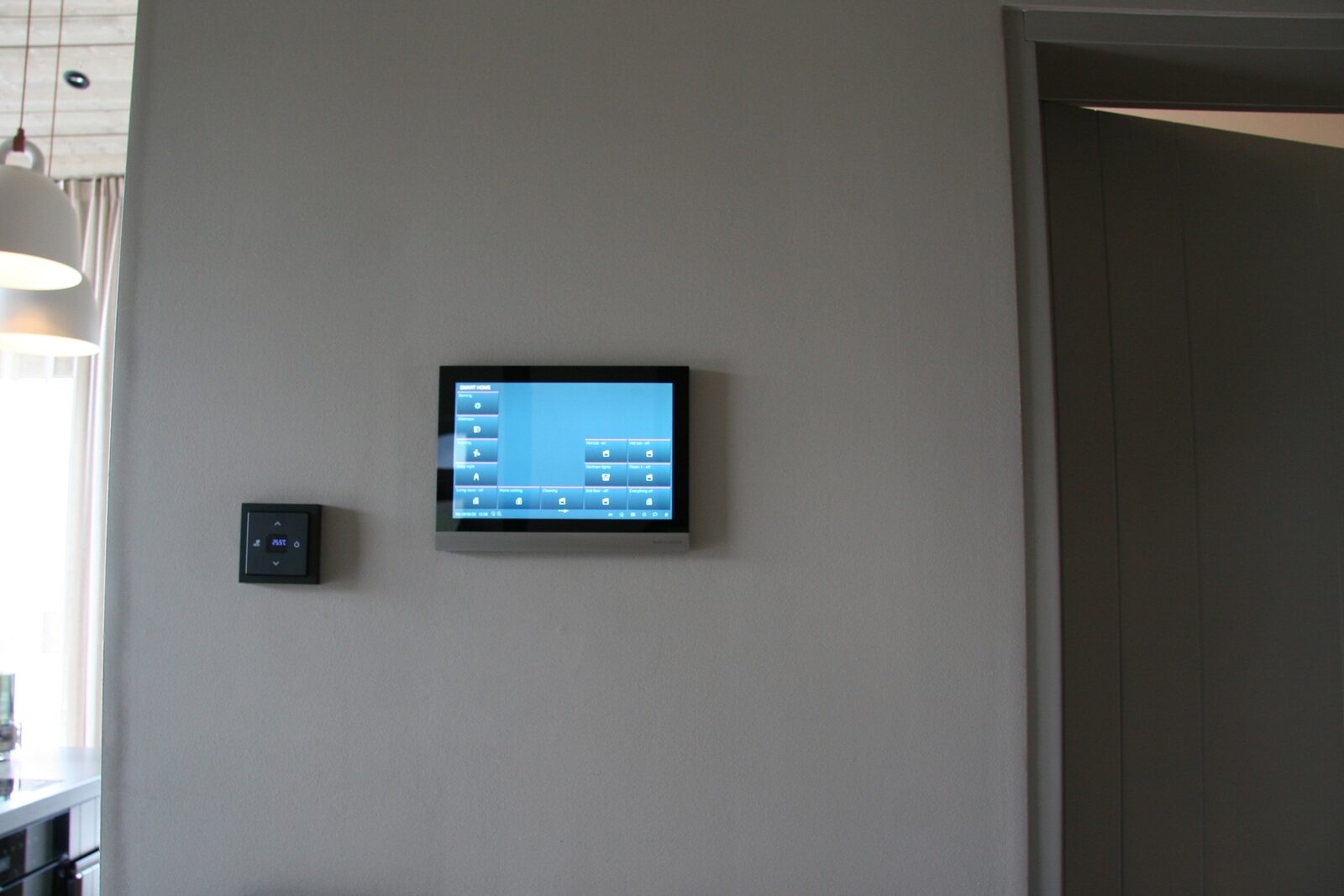 A wall-mounted touchscreen control panel for lighting and temperature, beside a hallway doorway.